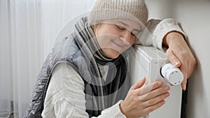 Young woman feeling very cold at home sitting by the heating radiator. Concept of energy crisis, high bills, broken heating system