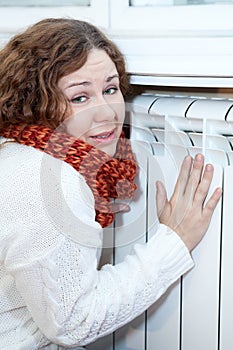 Young woman feels cold sitting near heating con