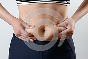 A young woman feels with two hands folds on her stomach. On light white background. Concept of weight loss, proper nutrition,