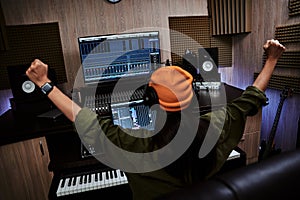 Young woman, female artist raising her arms while succeeding in creating music, sitting in recording studio