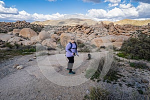 Young woman female hiker wearing a backpack starts off on a hiking trail in Joshua Tree National Park, to the Arch Rock