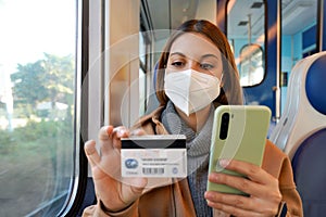 Young woman with FFP2 KN95 protective mask traveling with train paying with her credit card on smart phone for shopping online