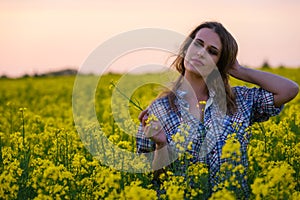 Young woman in a field of oil rapeseed in bloom in sunset. Freedom and ecology concept.