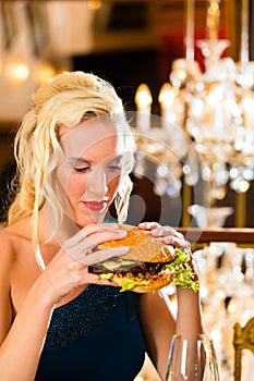 Young woman in fine restaurant, she eats a burger