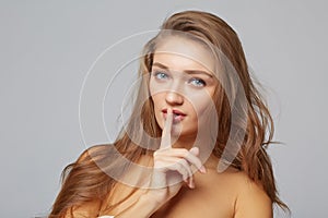 Young woman with finger on lips, on gray background