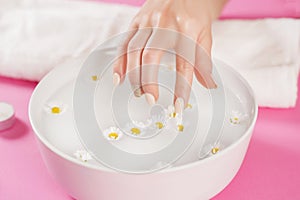 Young woman finger with nails polish touch daisy flower in water in bowl