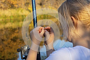 Young woman fisherman prepares to fish. Puts live bait worm on the hook of fishing rod with spinning reel. Close-up, selective