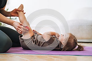 Young woman fit mom with baby girl doing exercises with massage ball on mat at home