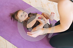 Young woman fit mom with baby girl doing exercises with massage ball on mat at home