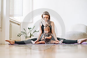 Young woman fit mom with baby girl doing fitness on mat at home
