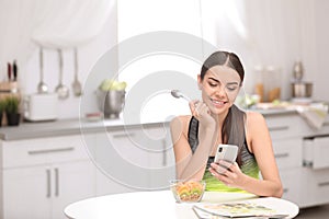 Young woman in fitness clothes using smartphone while having healthy breakfast at home