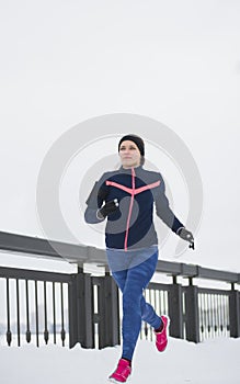 Young woman fitness model running at snow winter promenade