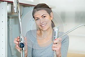 Young woman fixing sink pipe with adjustable wrench in kitchen