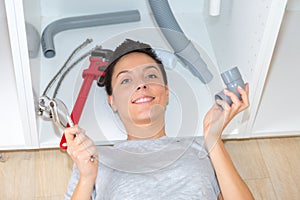 young woman fixing sink pipe with adjustable wrench in kitchen