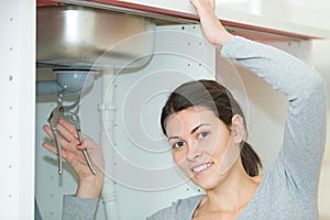 young woman fixing sink pipe with adjustable wrench in kitchen