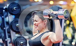 Young woman flexing muscles with dumbbell in gym
