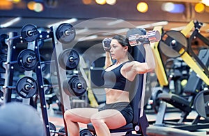 Young woman flexing muscles with dumbbell in gym