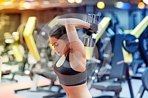 Young woman flexing muscles with dumbbell in gym