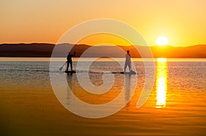 A young woman floats on a sapa on a mountain lake against the backdrop of sunset