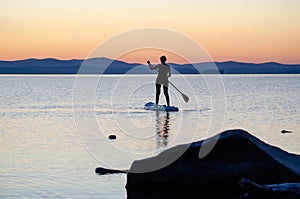 A young woman floats on a sapa on a mountain lake against the backdrop of sunset. Active recreation for a healthy lifestyle