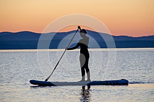 A young woman floats on a sapa on a mountain lake against the backdrop of sunset. Active recreation for a healthy lifestyle