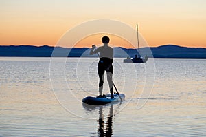 A young woman floats on a sapa on a mountain lake against the backdrop of sunset. Active recreation for a healthy lifestyle