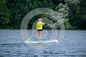A young woman floats on a SUP board along a large river. Swim on the board for amazing outdoor activities