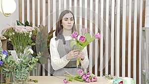 Young woman florist composing a bouquet of tulips in a flower shop or workshop.