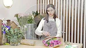 Young woman florist composing a bouquet of tulips in a flower shop or workshop