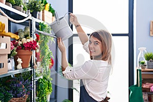 Young woman florist smiling confident watering plant at florist