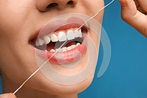 Young woman flossing her teeth on blue background, closeup. Cosmetic dentistry