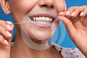 Young woman flossing her teeth on blue background, closeup. Cosmetic dentistry