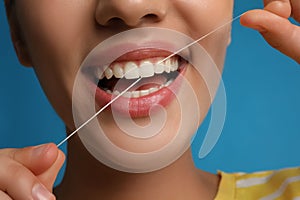Young woman flossing her teeth on blue background, closeup. Cosmetic dentistry