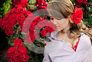 Young woman in flower garden smelling red roses