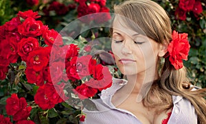 Young woman in flower garden smelling red roses