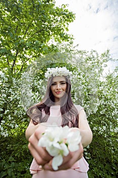 Young woman in flowers wreath in spring blossom park outdoors. Beautiful girl outdoor portrait on foliage background