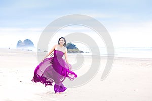 Young woman in flowing magenta dress standing on beach