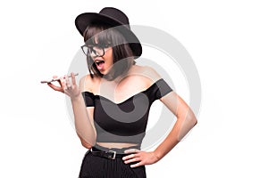 Young woman in fluppy black hat and black clothes shout on phone on white background