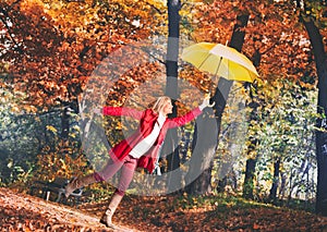 Young woman flying in the autumn park with yellow umbrella