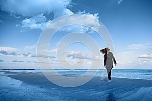 Young woman with flying hair standing on beach near the sea. Spacious sky with clouds. Harmony of man and nature, freedom concept