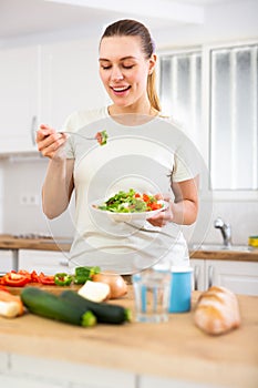 Young woman following healthy diet eating vegetable salad in kitchen