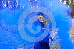 Young woman in forest having fun with blue smoke grenade, bomb