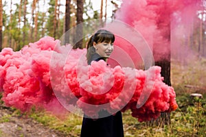 Young woman in forest having fun with red smoke grenade, bomb