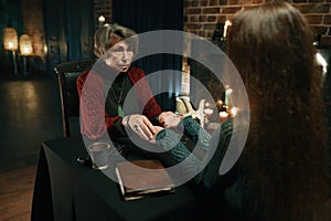 Young woman at fortune teller chiromancer consultation side view shot