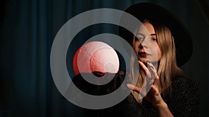 A young woman fortune teller in a hat is holding a magic ball.