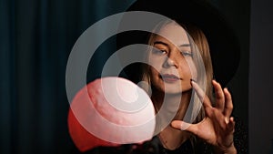 A young woman fortune teller in a hat is holding a magic ball.