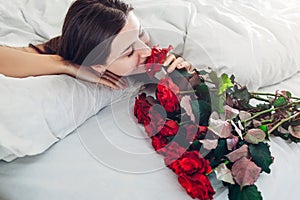 Young woman found bouquet of roses in bed. Happy girl smelling flowers. Women`s day