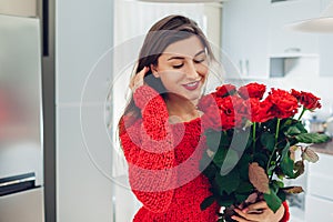 Young woman found red roses on kitchen. Happy girl smelling flowers. Women`s day