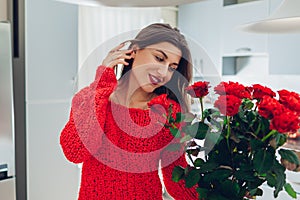 Young woman found red roses on kitchen. Happy girl smelling flowers. Women`s day