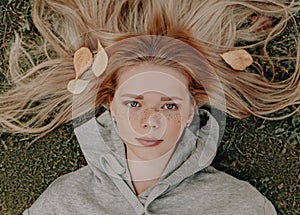 Young woman with freckles on her face laying in the park, leafs on her hair